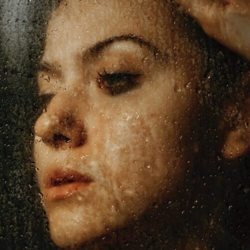 melancholic woman with makeup behind wet glass wall