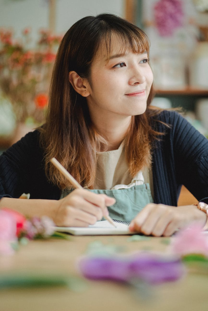 positive asian woman drawing in notebook with pencil